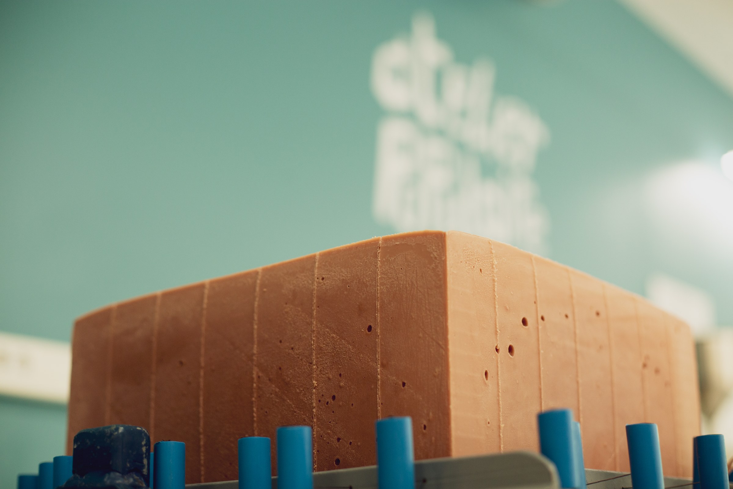 Un bloc de savon à froid posé sur la table de découpe de l'atelier, devant le mur bleu canard au logo Atelier Populaire.