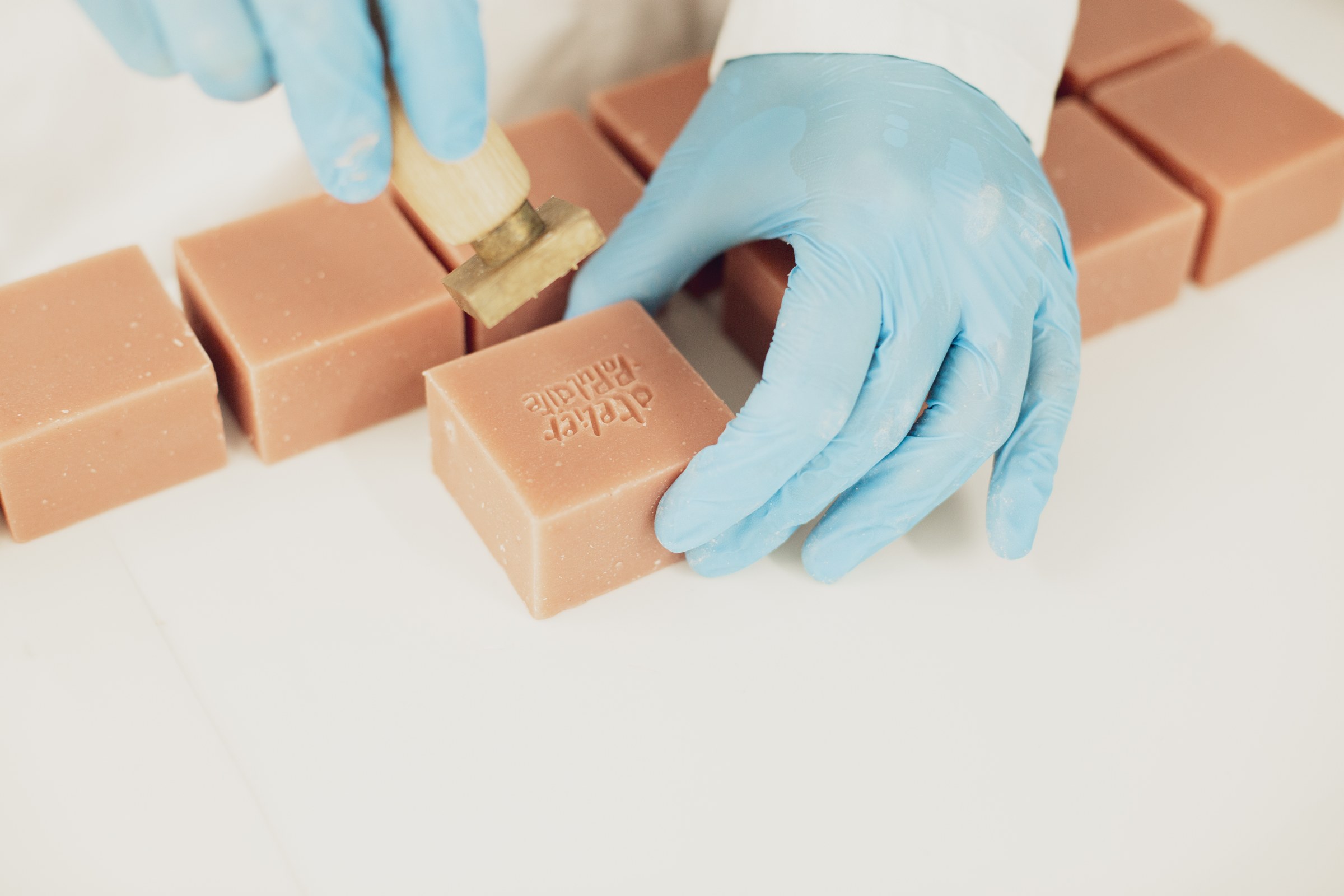 Main gantée qui appose le tampon en laiton Atelier Populaire sur un pavé de savon rose.